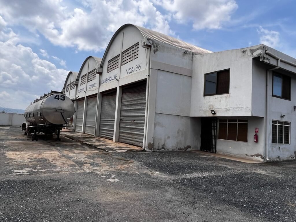 Large commercial warehouse facility with multiple rolling shutter bays, attached office blocks, and a spacious paved logistics yard.