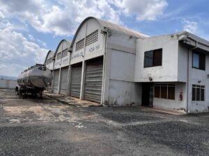 Large commercial warehouse facility with multiple rolling shutter bays, attached office blocks, and a spacious paved logistics yard.